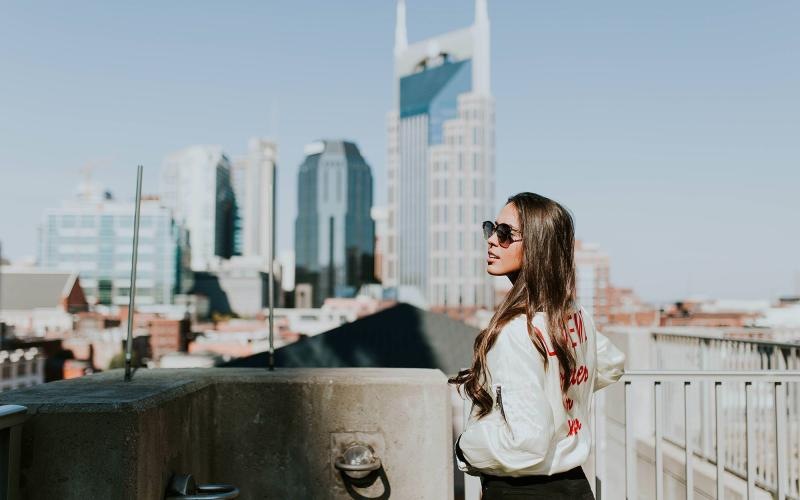 woman with sunglasses stands on a rooftop overlooking the city